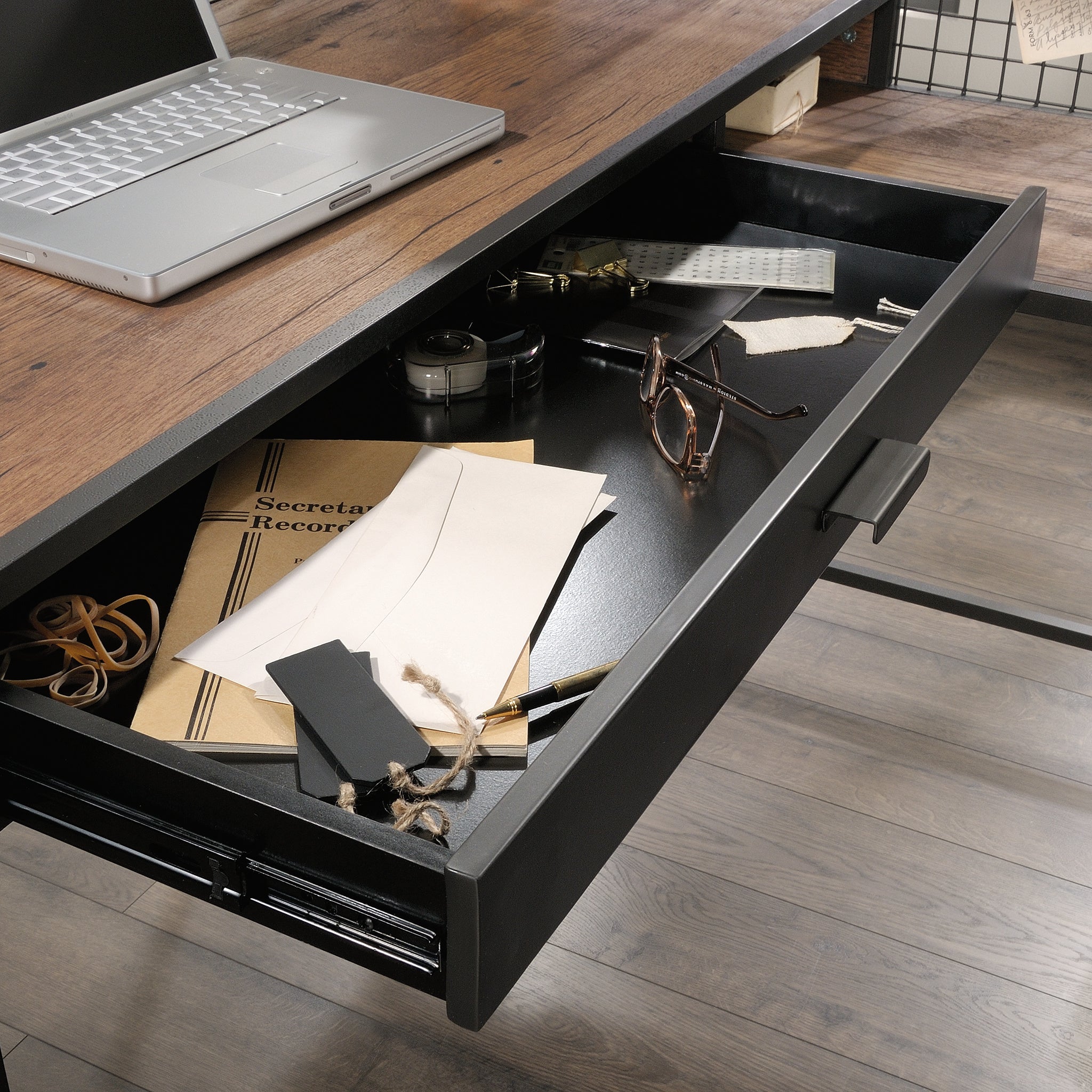 Wide drawer of L-shaped computer desk, brown finish, open to reveal storage for documents and accessories in industrial office furniture.