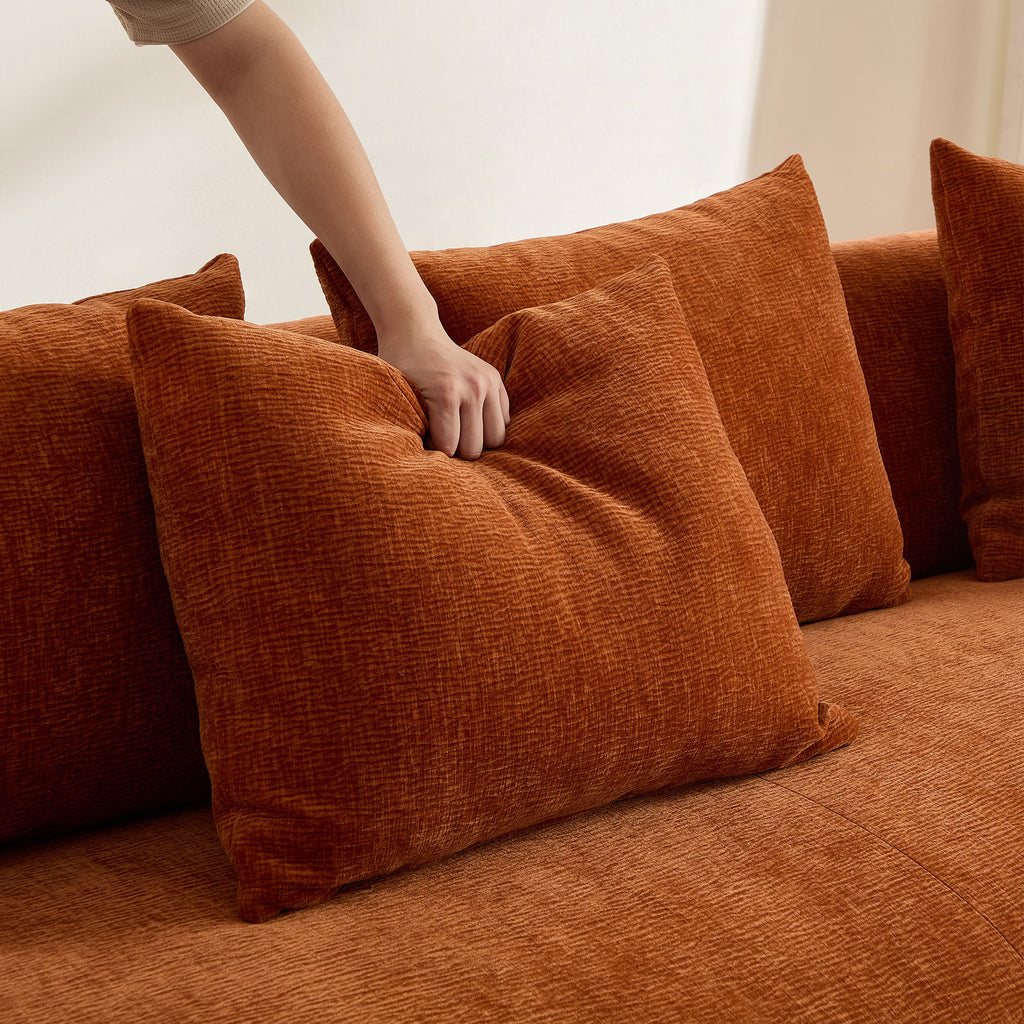 Hand pressing into plush orange back cushion of the oversized L-shape sectional sofa, demonstrating softness and comfort.