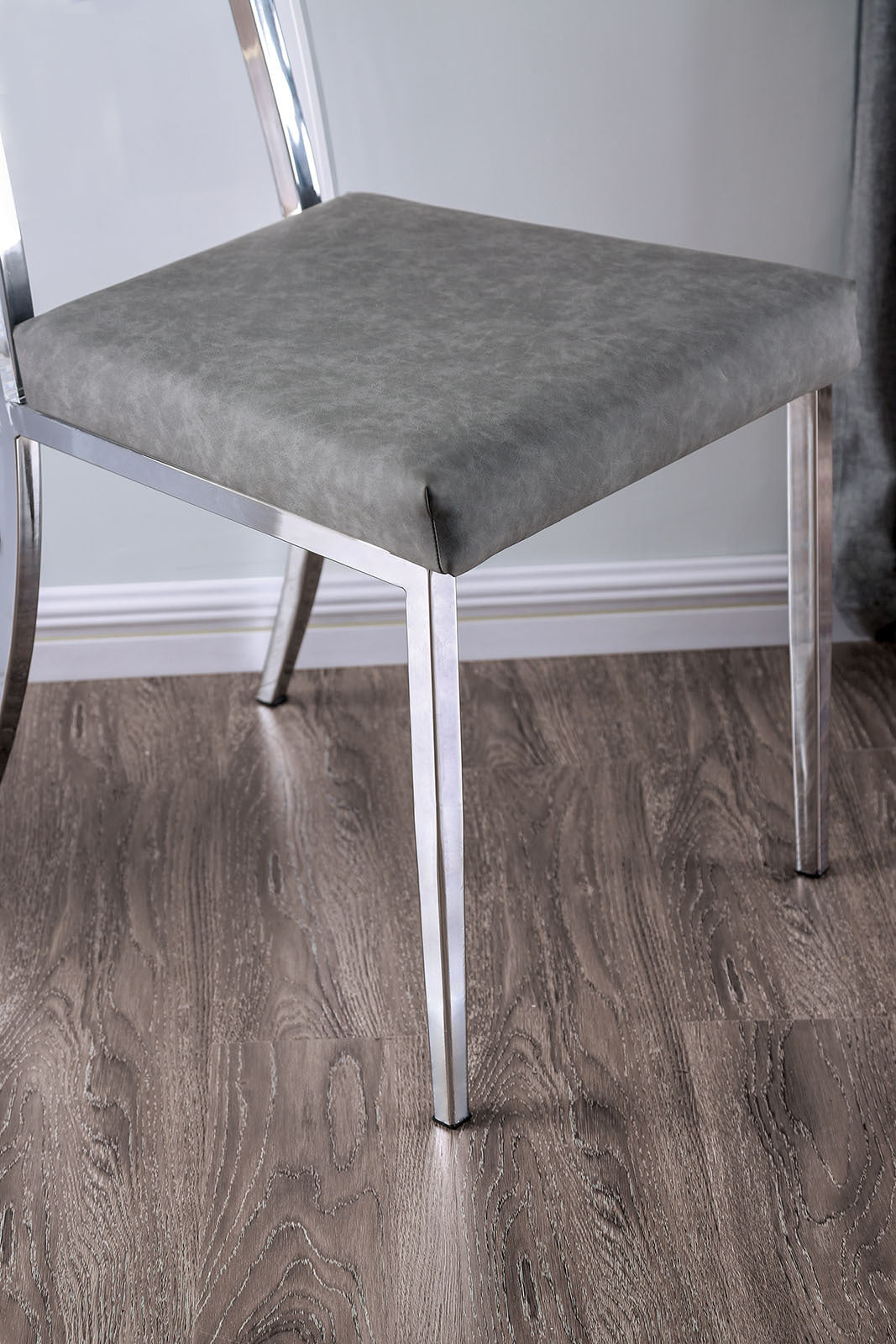 Close-up of minimalist dining chair's chrome legs and gray cushioned seat, showcasing sleek modern design details.