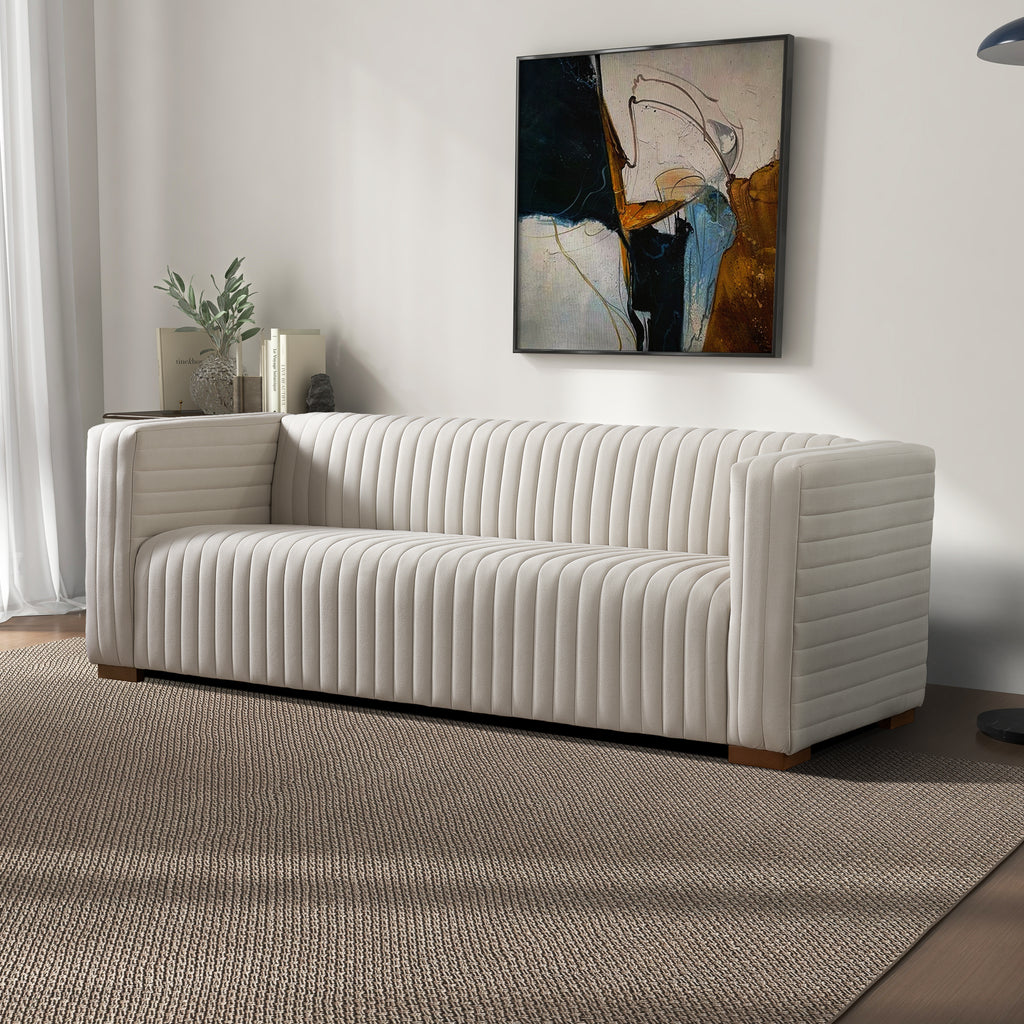 Elara cream velvet sofa featuring vertical channel tufting and a modern, minimalist silhouette on a textured area rug.