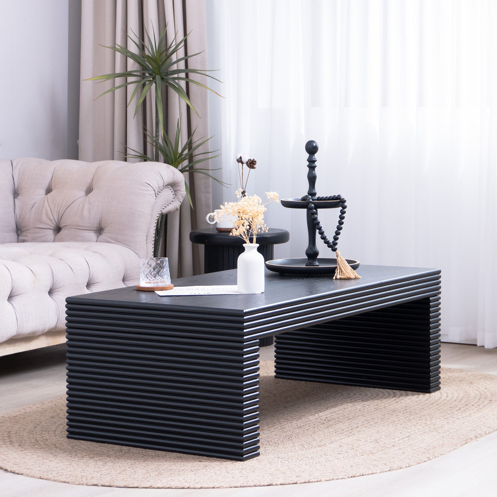 Contemporary black ribbed coffee table placed on a woven rug in a cozy living room, complementing neutral-toned furniture.