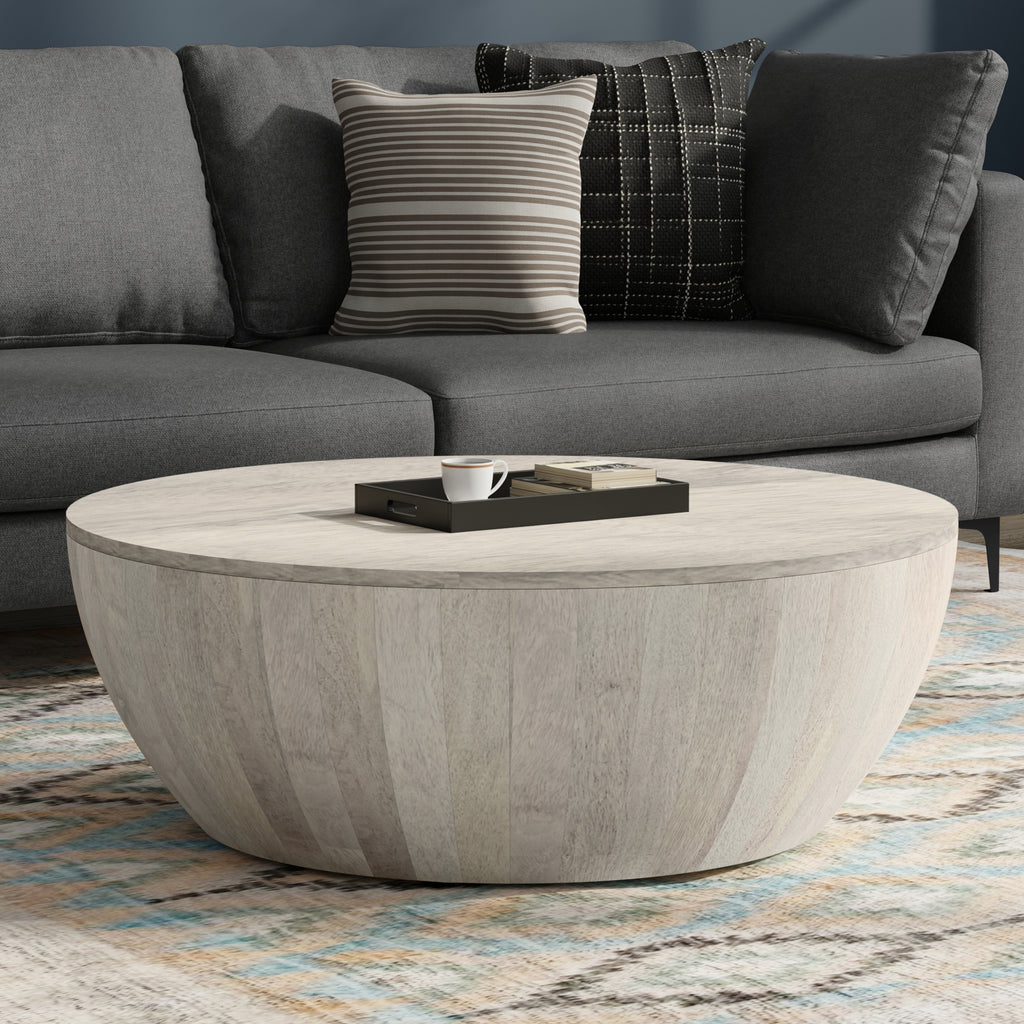 Elmbrook Drum Coffee Table in rustic white wood placed in a modern living room with a gray sofa and patterned rug. Ideal for coastal or contemporary decor.