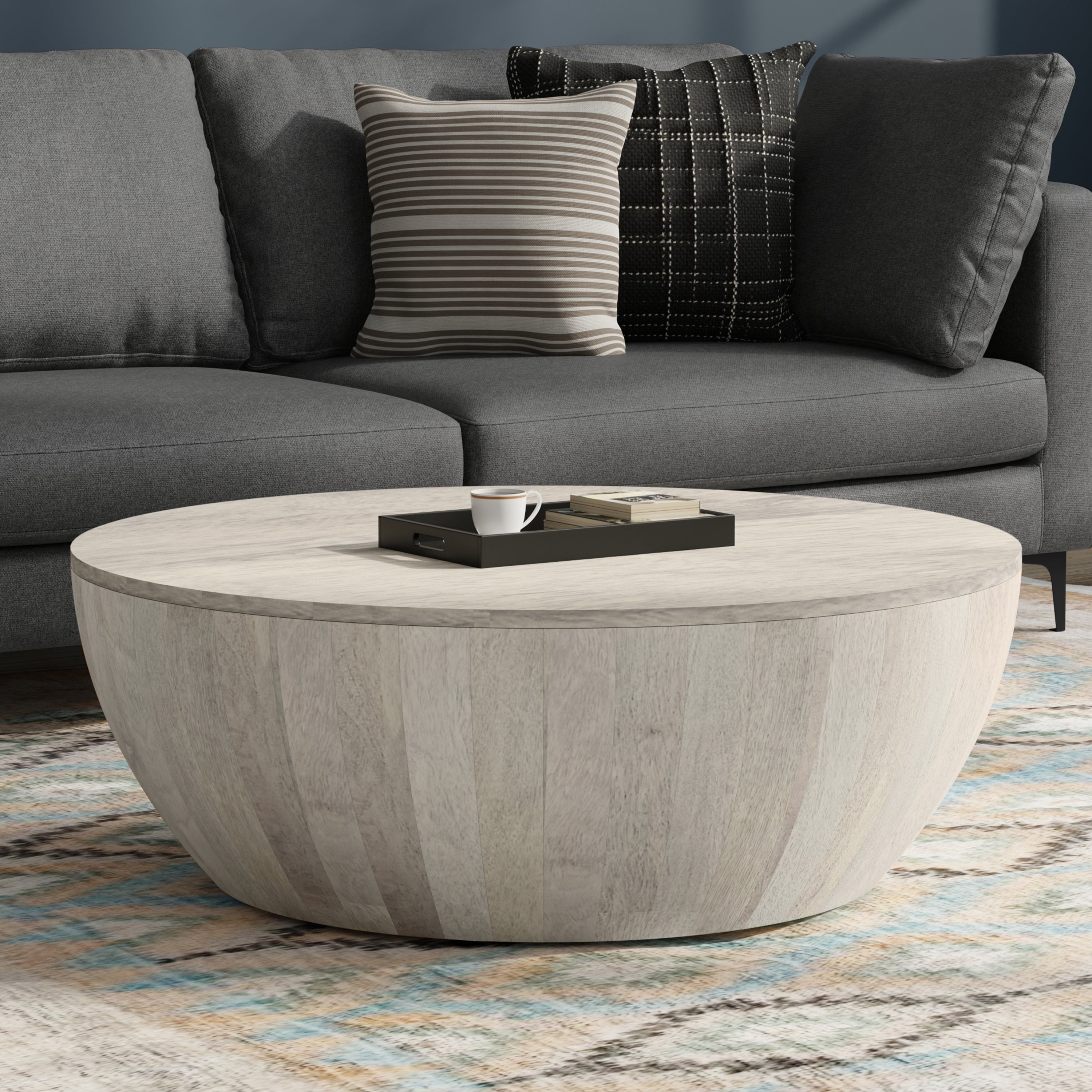 Elmbrook Drum Coffee Table in rustic white wood placed in a modern living room with a gray sofa and patterned rug. Ideal for coastal or contemporary decor.