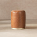 Round camel brown leather ottoman stool with a modern silhouette and a sleek metallic base.