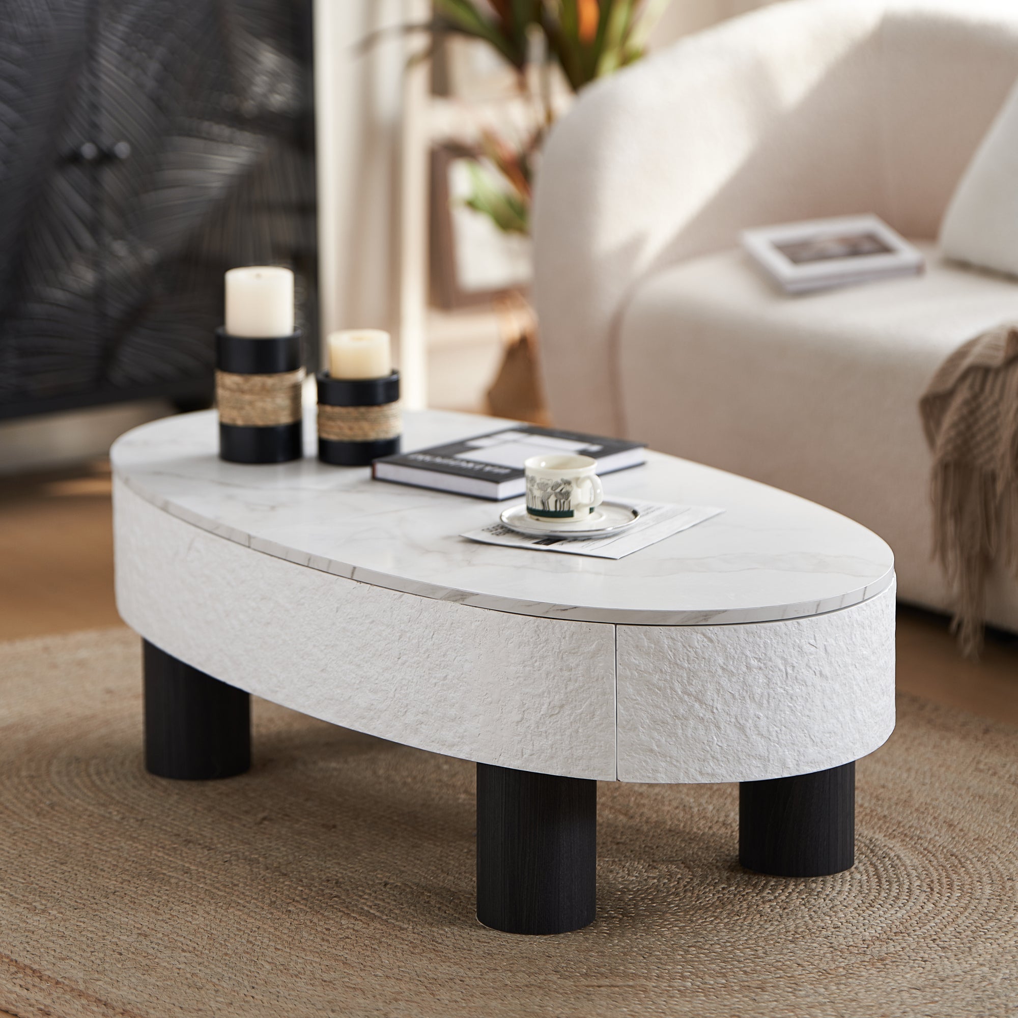 Oval coffee table with faux marble surface and hidden storage, styled with candles and books in a modern living room setting.