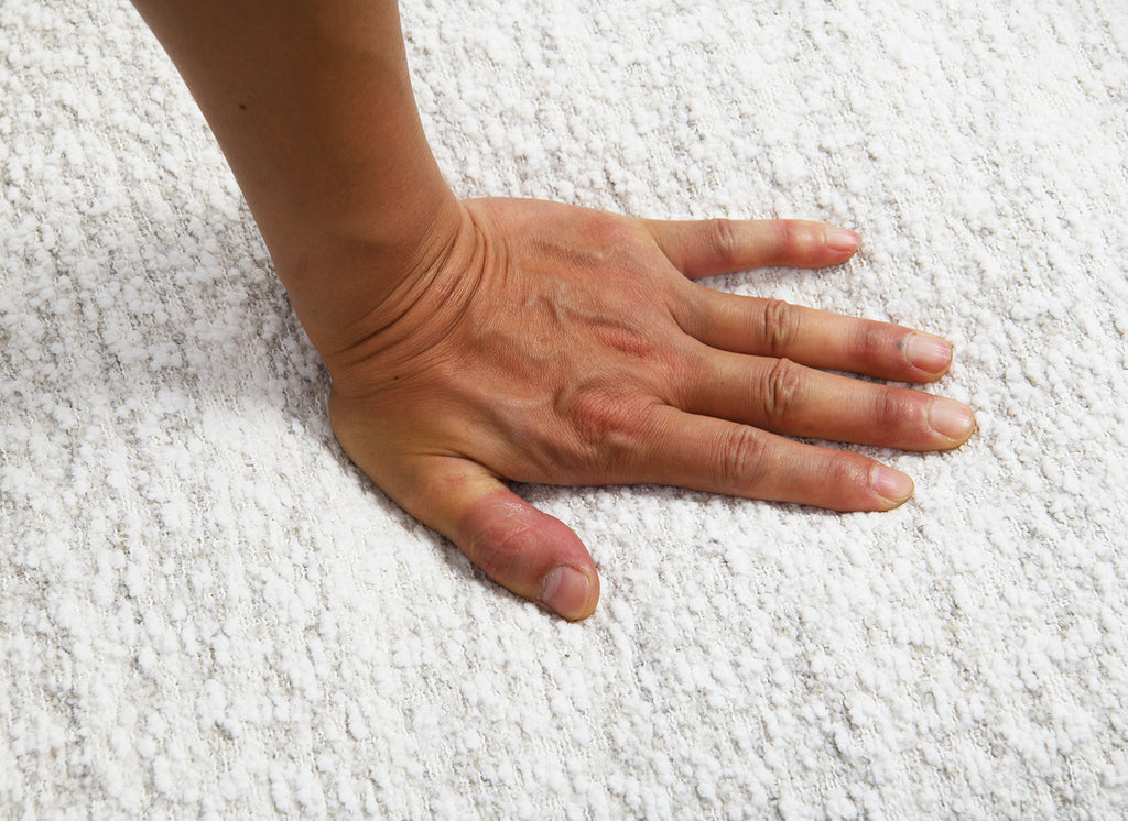 Hand pressing into the soft boucle fabric of the White Swivel Chair Contemporary, demonstrating its plush cushioning and premium comfort.