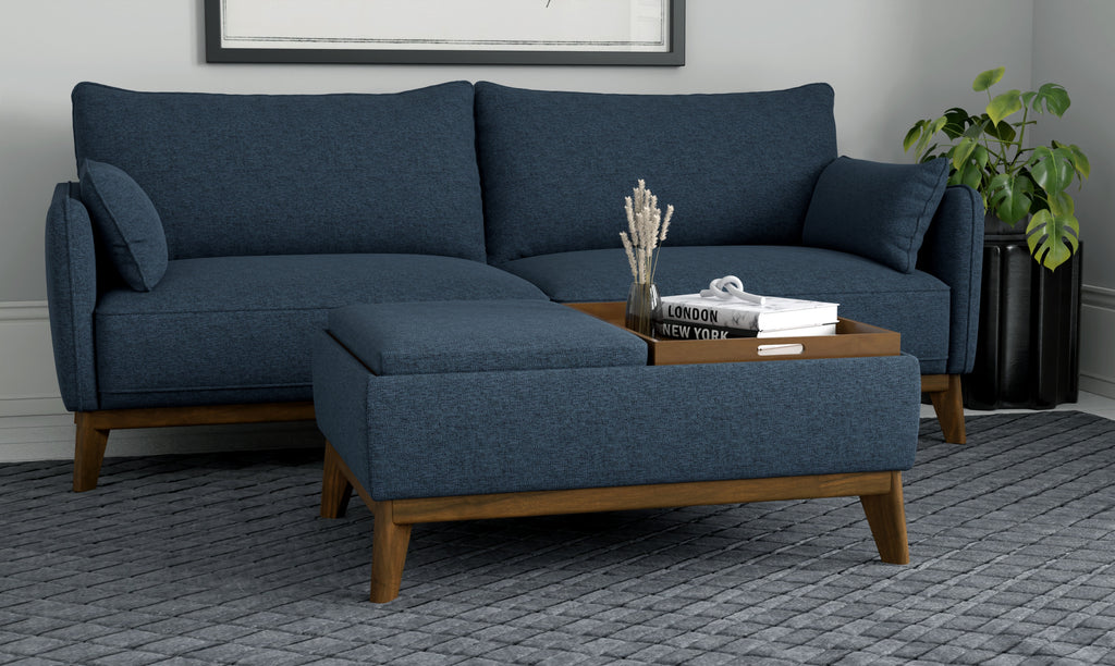 Blue fabric ottoman with tapered wooden legs and a reversible wood tray top, placed in front of a matching blue sofa.