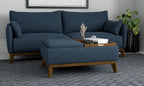 Blue fabric ottoman with tapered wooden legs and a reversible wood tray top, placed in front of a matching blue sofa.