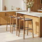 Sven 30' modern low back wood barstools in dark brown walnut ash wood placed at a kitchen island with white countertop and wood cabinetry.
