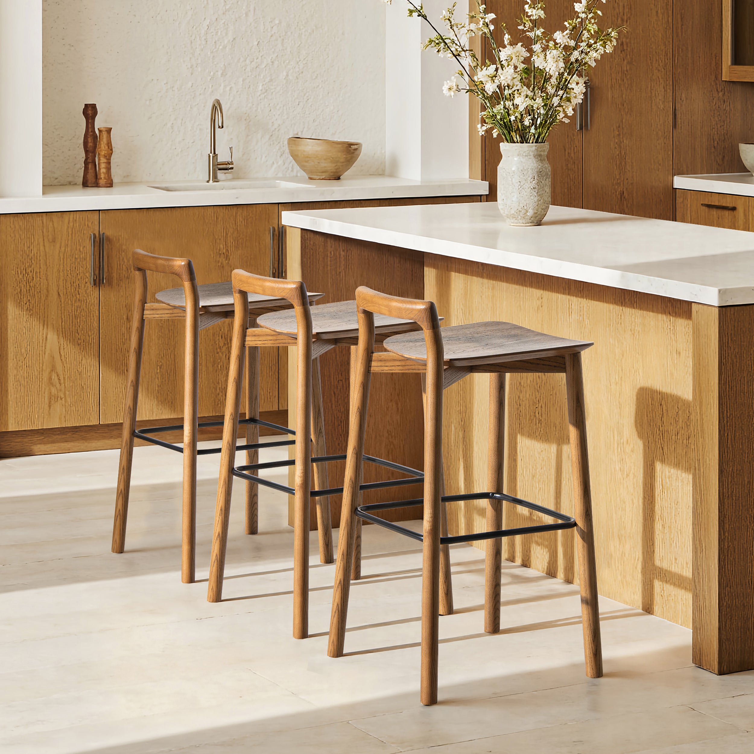 Sven 30' modern low back wood barstools in dark brown walnut ash wood placed at a kitchen island with white countertop and wood cabinetry.