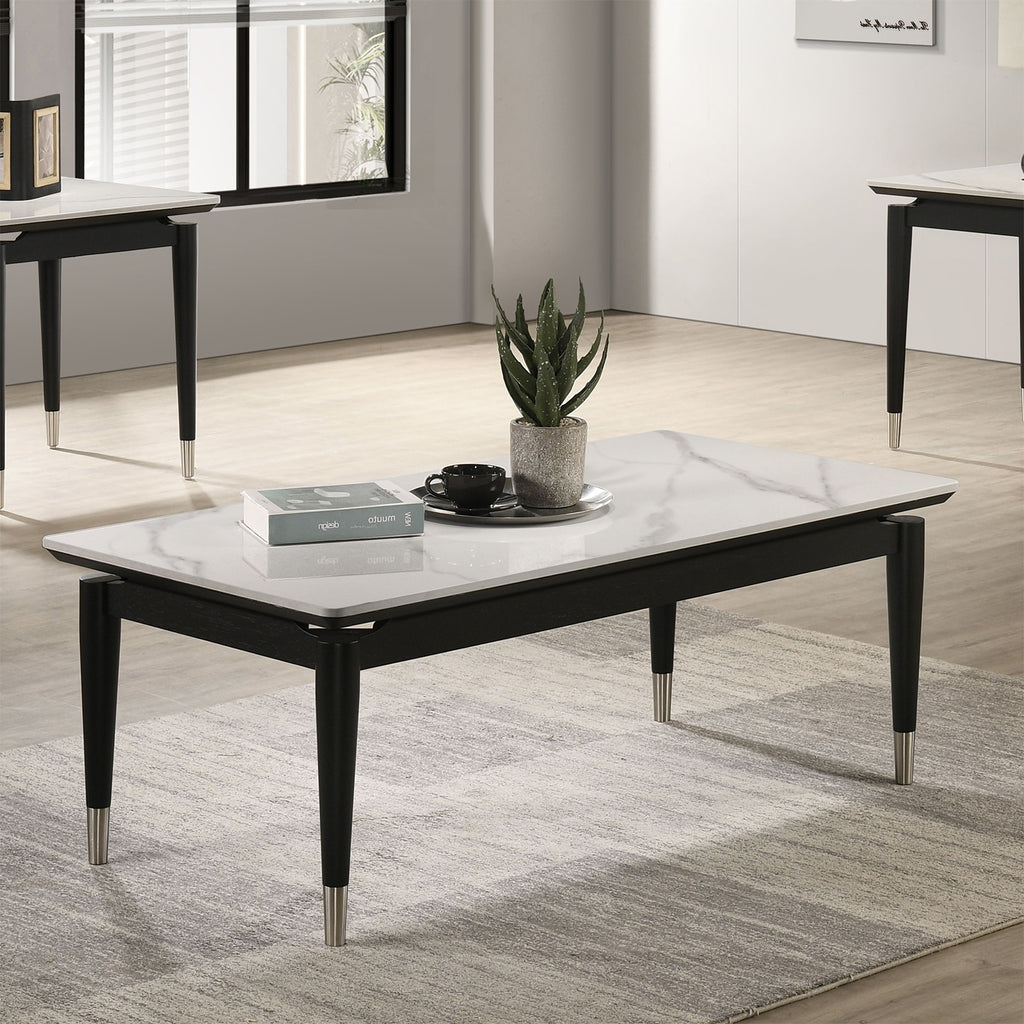 Modern black and white coffee table with sintered stone top and metal accents, placed on a rug in a bright, minimalist living space.