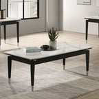 Modern black and white coffee table with sintered stone top and metal accents, placed on a rug in a bright, minimalist living space.