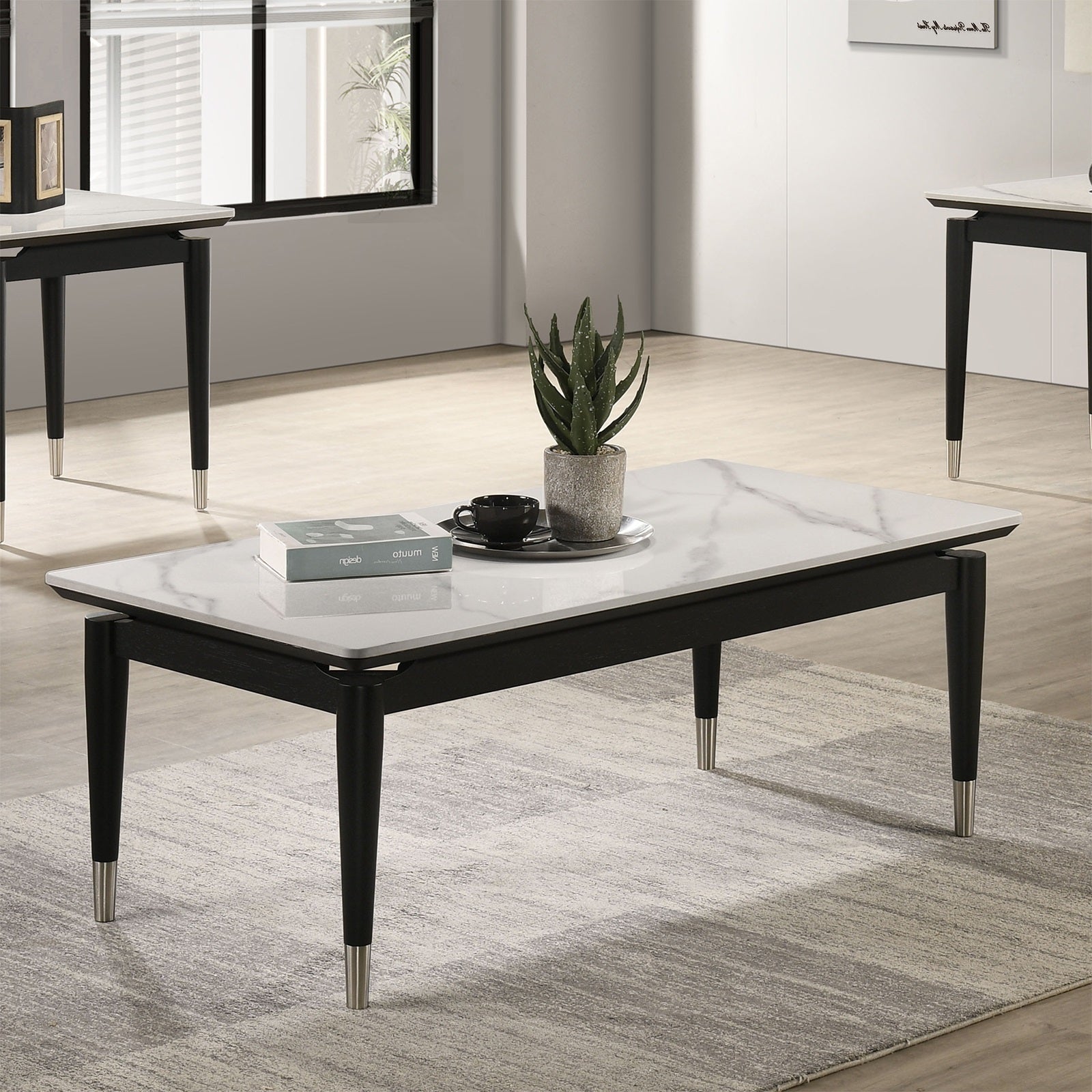 Modern black and white coffee table with sintered stone top and metal accents, placed on a rug in a bright, minimalist living space.