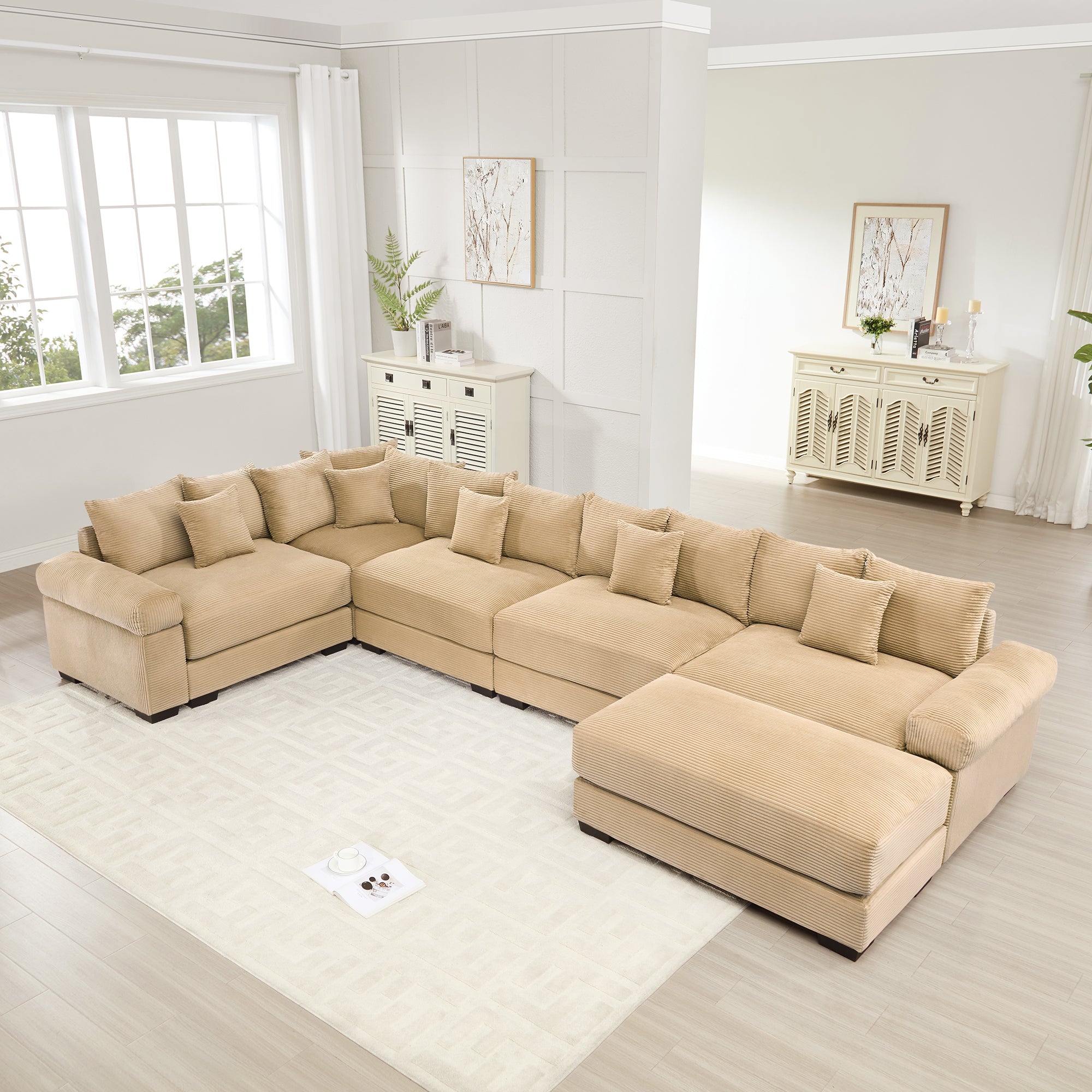 Oversized camel corduroy modular sectional sofa with extra-wide armrests and matching ottoman in a bright living room.