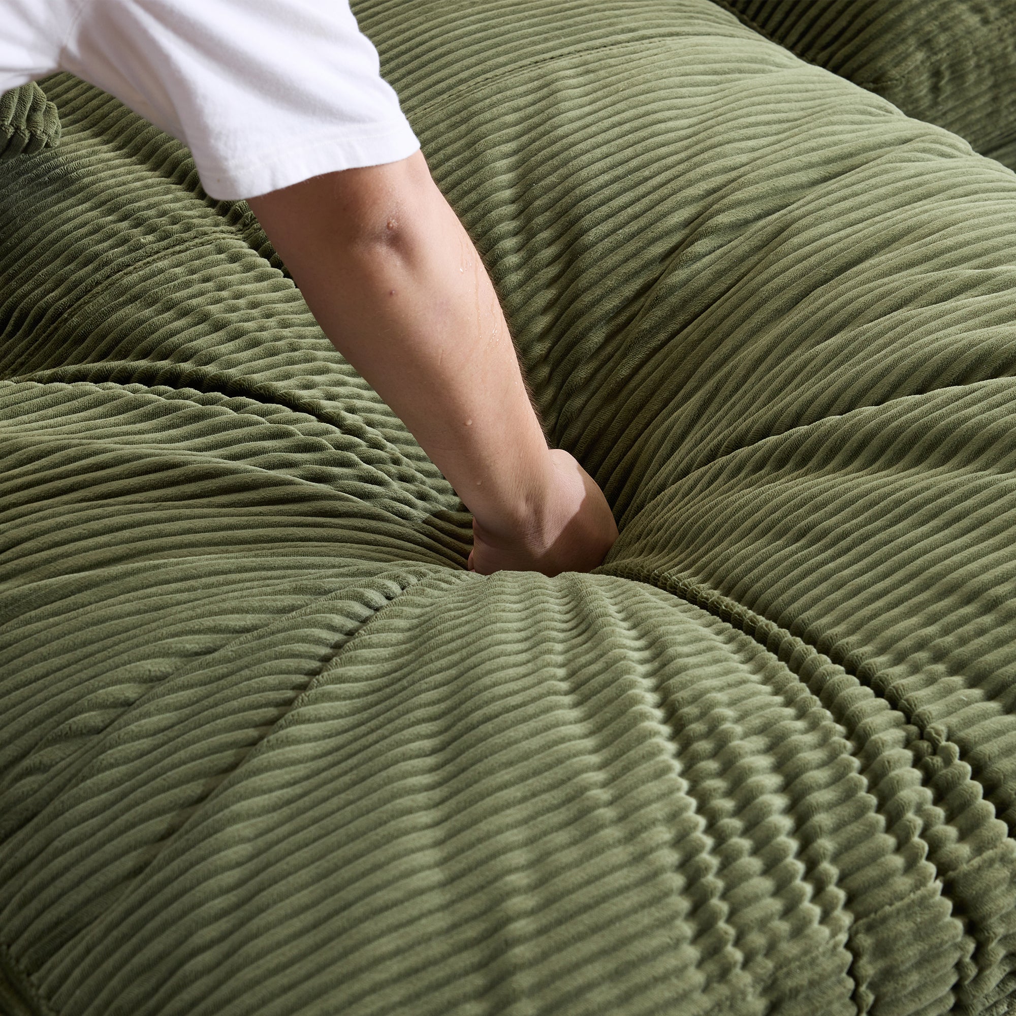 Hand pressing into green corduroy foam-filled cushion, demonstrating the plush softness and comfort of the sofa's seat padding.